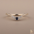 Delicate gold ring with a blue gemstone and smaller diamonds on a beige background