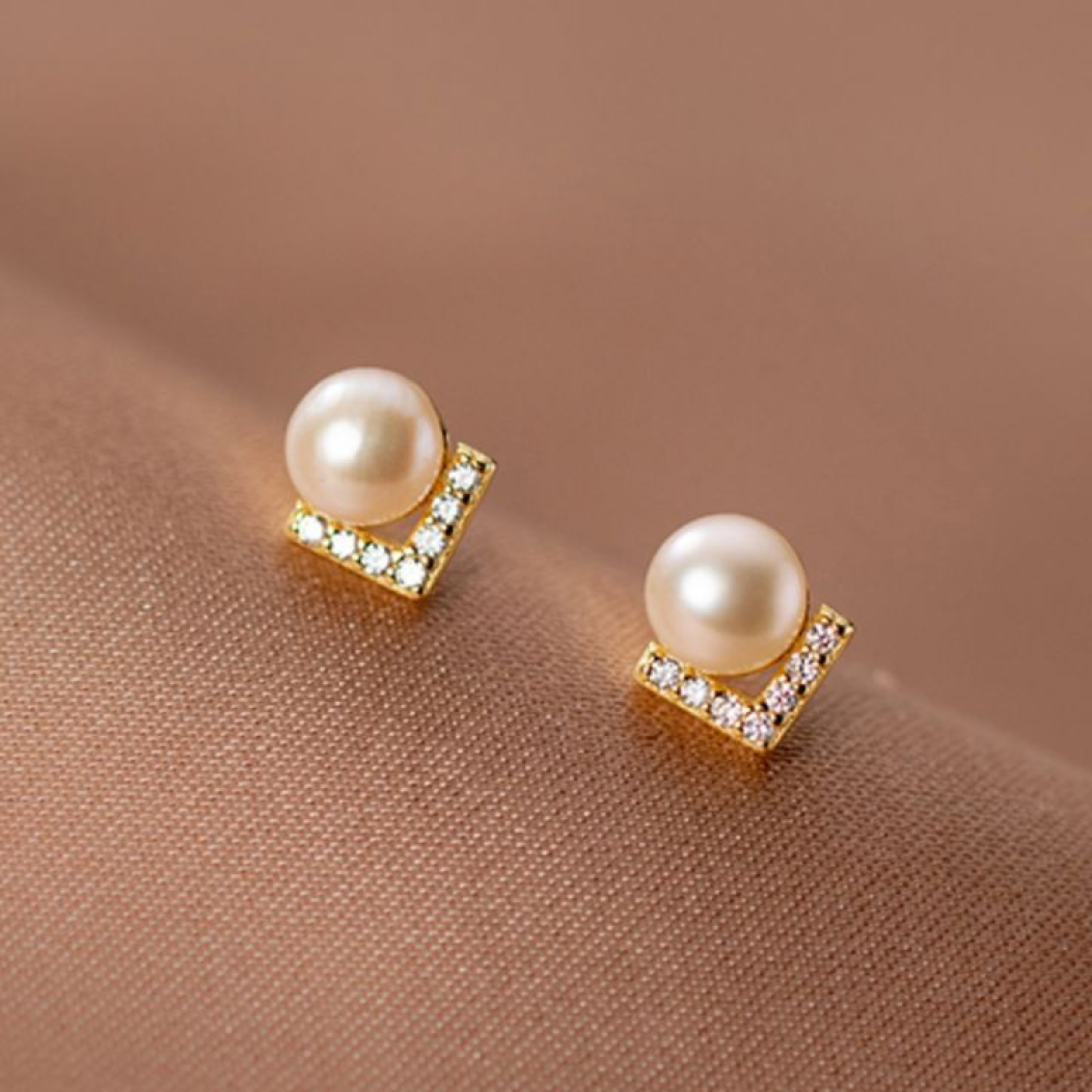 Pearl earrings with gold accents on a brown fabric background