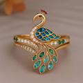 Gold peacock-shaped ring with gemstones on a beige background